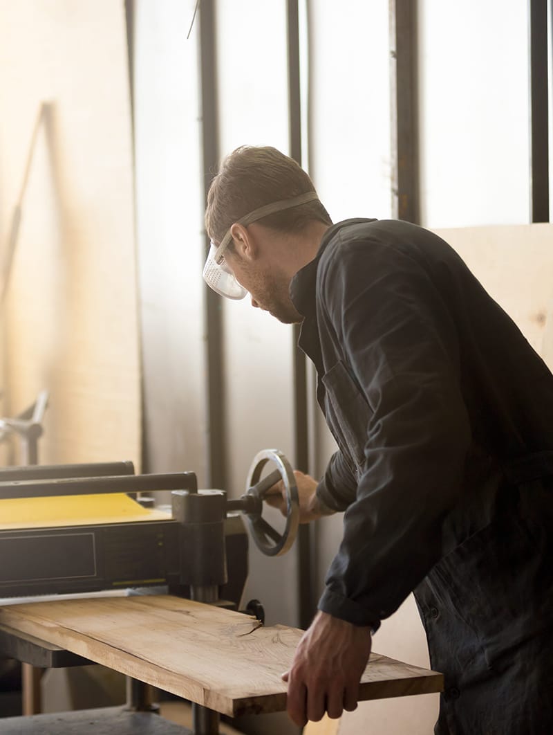 Worker operating stationary power planer, processing wooden boar